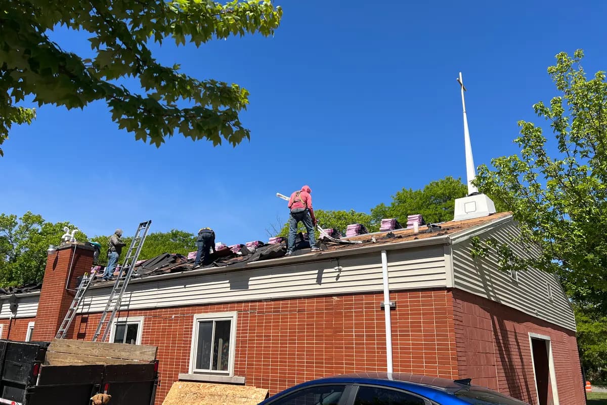 Apexium Roofing crew tearing off the roof of a historic brick building with a steeple near Cedarburg, WI