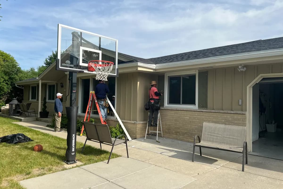 Apexium Roofing crew on a ladder at a Glendale, WI ranch home with a driveway basketball hoop